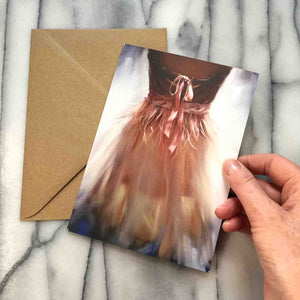 
                  
                    Load image into Gallery viewer, Ballerina Greeting Card, view of a pink organza dress with ribbons and bow against a glowing background, shown with envelope.  Posed with hand for scale.
                  
                