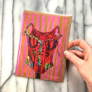 
                  
                    Load image into Gallery viewer, BUSTIER! Greeting Card is brightly coloured and whimsical with red, pink, blue, lime, yellow, based on 18th century corset, front view, 7&amp;quot; x 5&amp;quot;, with envelope in a protective plastic sleeve shown with hand to demonstrate size
                  
                